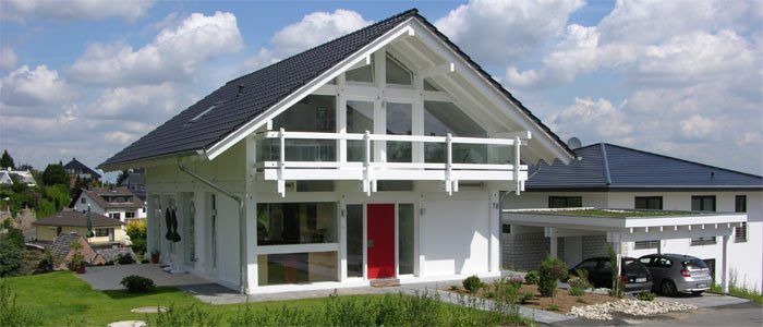 Weißes Holzfachwerkhaus mit Giebelbalkon und roter Haustür