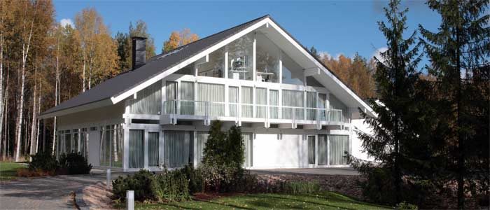 Weiße Villa mit großem Giebel und verglaster Fassade zwischen Birken und Tannen